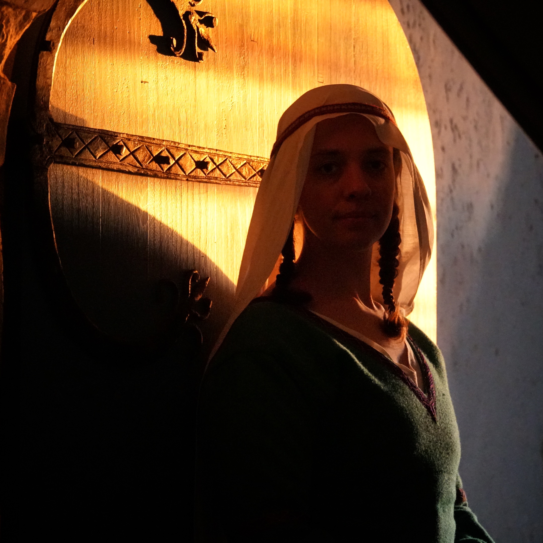 A high status medieval woman is silhouetted in the doorway of a castle by the setting sun