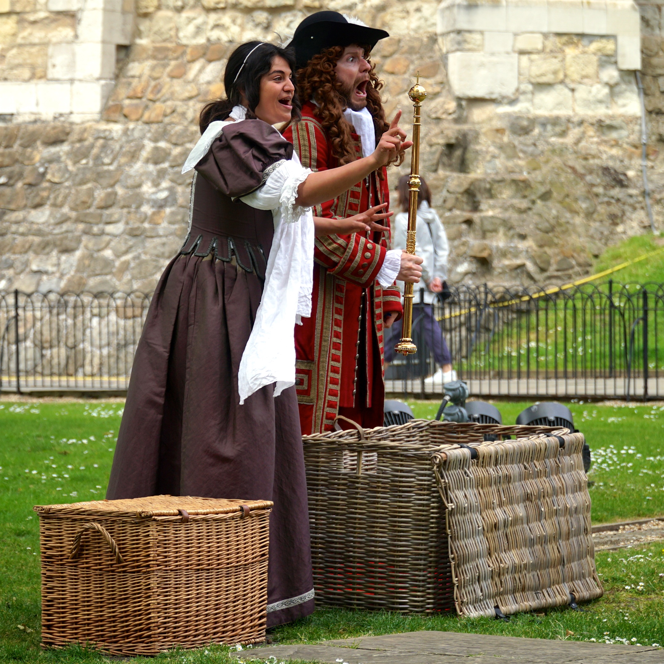 A high-status Restoration man and woman stand in front of the Tower of London looking shocked at having found the Crown Jewels in a wicker basket